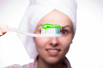 young woman in a towel on her head holding a toothbrush with toothpaste in her hand