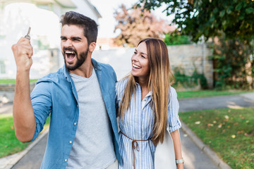 Beautiful happy young couple standing together outside in front of their new home.