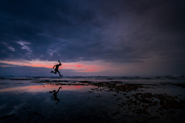 The silhouette of a man jumping at the beach and his shadow being reflected on the water, Limon, Costa Rica.