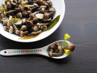 Delicious, beautiful, small pickled mushrooms in a dessert spoon close-up. Home recipe - delicious pickles with garlic, pepper, Bay leaf, cherry leaf and herbs in a white plate on a wooden table.