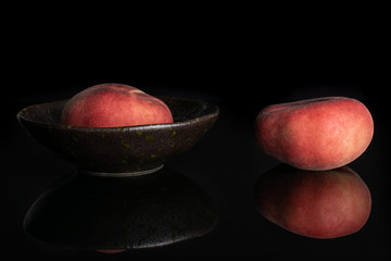 Group of two whole fresh red peach prunus persica platycarpa in dark ceramic bowl isolated on black...
