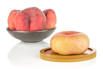 Group of four whole fresh red peach prunus persica platycarpa in dark ceramic bowl on round bamboo coaster isolated on white background