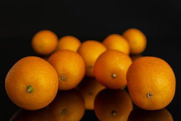 Lot of whole fresh orange kumquat arranged symmetrically isolated on black glass