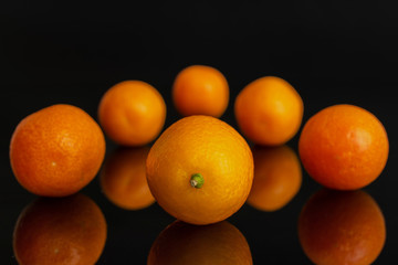 Group of six whole fresh orange kumquat one is in the front arranged symmetrically isolated on black glass