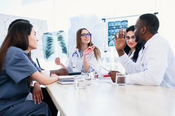 International team of young doctors discussing x rays result in the clinic. Showing patients...