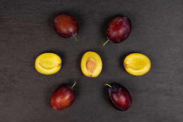 Group of four whole three halves of fresh blue plum arranged in a mandala flatlay on grey stone