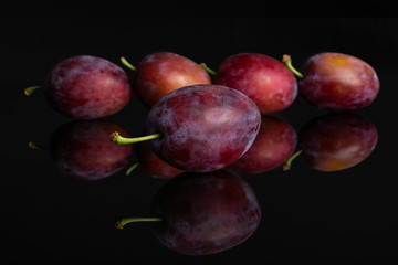 Group of five whole fresh blue plum isolated on black glass