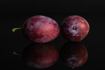 Group of two whole fresh blue plum isolated on black glass