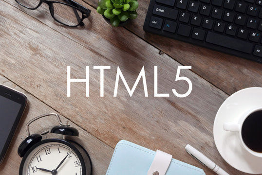 Top view of keyboard,plant,sunglasses, a cup of coffee,pen,notebook,clock and mobile phone on wooden background written with HTML5.