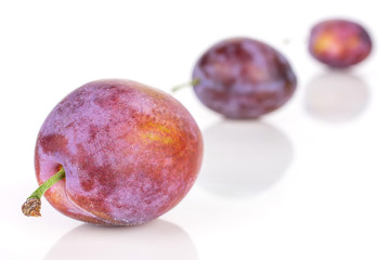 Group of three whole fresh blue plum placed diagonally in line isolated on white background