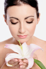 Fototapeta premium Beautiful young woman with lilly flower portrait. Young girl holding flower in her hands. Spa skin care.