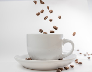 Coffee beans fall into a white porcelain cup and saucer, bouncing and jumping through the air conveying alert excitement, all isolated against a white background