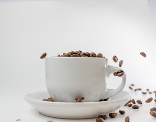 Coffee beans fall into a white porcelain cup and saucer, bouncing and jumping through the air conveying alert excitement, all isolated against a white background