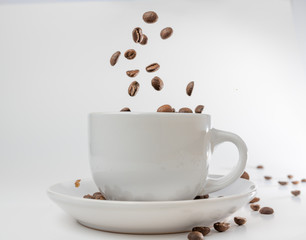 Coffee beans fall into a white porcelain cup and saucer, bouncing and jumping through the air conveying alert excitement, all isolated against a white background