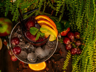 Naklejka na ściany i meble Red alcoholic cocktail in a bucket with ice. Garnished with fruits and berries on a wooden table.