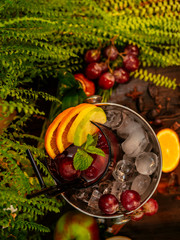 Red alcoholic cocktail in a bucket with ice. Garnished with fruits and berries on a wooden table.