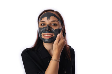 A young woman inflicts a black mask on the face isolated on white background.The concept of healthy lifestyle, beauty, body care.