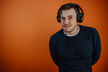 A beautiful young man in headphones with ears is dancing on an orange background. The concept of International Music Day.