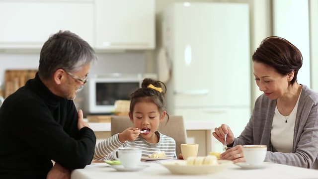 Grandparents with granddaughter eating cake and talking at home