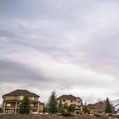 Square frame Vast cloudy sky over residential area built on snowy hill with coniferous trees