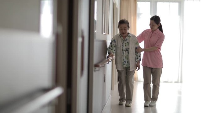 Caregiver helping senior woman walk along handrail
