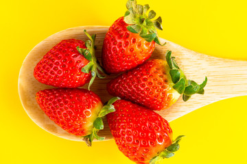 strawberries in a wooden spoon and yellow background