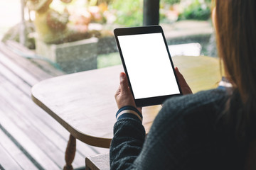 Mockup image of a woman sitting and holding black tablet with blank white desktop screen