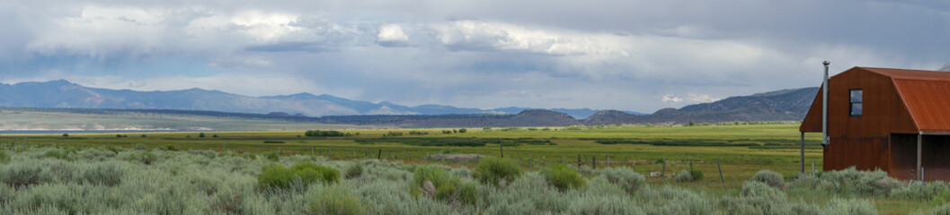 Red farm shed in a big grassland farm field with the mountain on the background.  Eastern Sierra Mountains, Mono County, California, USA