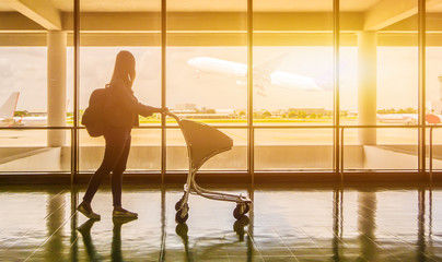 silhouette of a girl walkingsilhouette of a girl walking at the airport glass window, girl tourist hold bag and waiting near luggage in hall airplane departure. Travel Concept.