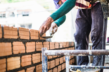 Close up of bricklayer worker's hand installing red brick with trowel putty knife for new house...