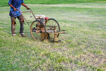 Fototapeta na wymiar Worker cutting grass with old lawn mower in the field in the evening. Static shot.