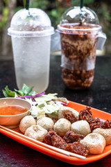 Thai fried meat balls served with spicy dipping chili sauce and vegetable with drinks in the background. Popular appetizers side dish roasted meat balls. Thai street food.
