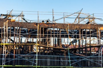Burned down wooden residential apartment, house, or condo complex exterior after construction site fire. Charred frame and walls, burnt roof and construction scaffolding