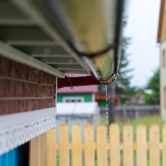 The bottom of the gutter under the edge of the roof in the new house of rural Yakutia with raindrops in wet weather. Collection of drinking water of the Northern peoples.
