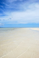 Soft waves of clear water on a clean sandy beach. Above the horizon, an intense blue sky with some clouds - Philippines, Asia.            