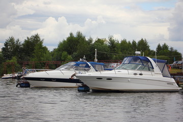 Beautiful two white modern inboard motor boats with blue awning at the pier on the river on the background of trees