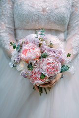 Stylish bride in a white dress holds an unusual wedding bouquet close-up. Delicate wedding bouquet of different flowers in the hands of the bride, selective focus.