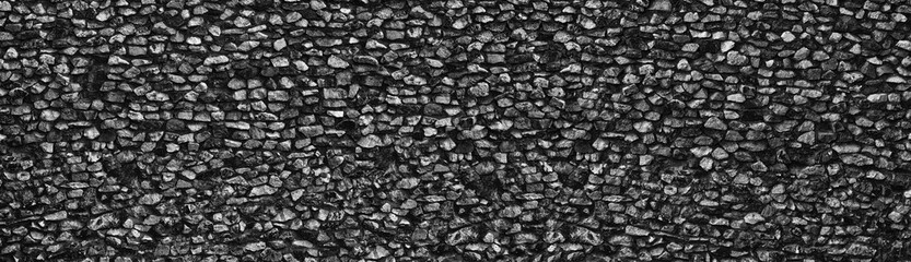 Black crushed granite stone wall wide texture. Rough rock long backdrop. Dark gray panoramic background