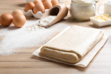 Parchment with puff pastry dough on wooden table, space for text