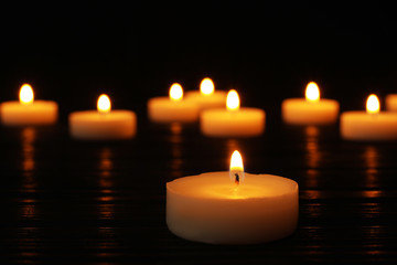 Burning candle on black table against blurred background, space for text