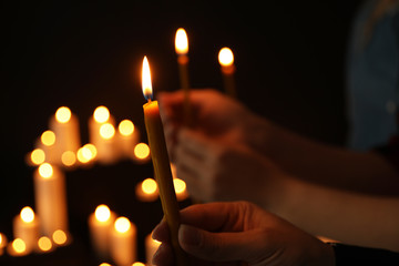 Woman holding burning candle in darkness against blurred background, closeup
