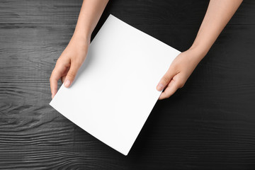 Woman holding blank paper sheets for brochure at black wooden table, top view. Mock up