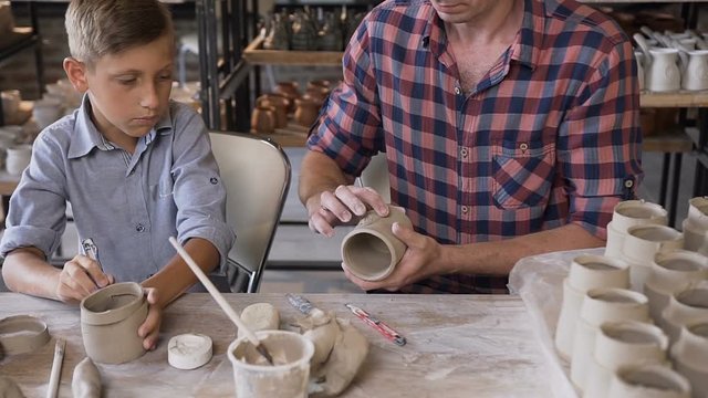 Little cute boy with his father making ceramic pots in the pottery.