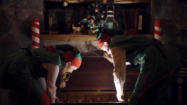 Surprised elves open the big chest in darkness. Santa's helpers elves open magic chest and taking beautiful box on Christmas decor background.
