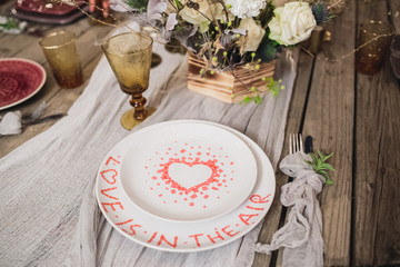 Romantic dinner of the bride and groom on a wooden table with plates and fresh flowers. 