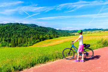 Young woman standing with bike on cycling way in green summer landscape near Czorsztynskie lake and Niedzica village, Pieniny Mountains, Poland