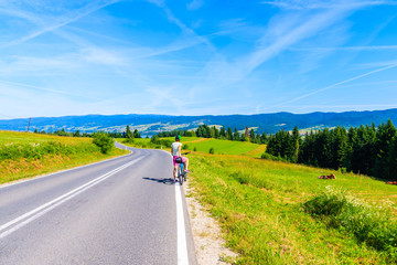 Young woman cyclist stopping on road and looking at Czorsztynskie lake on beautiful summer day, Pieniny Mountains, Poland