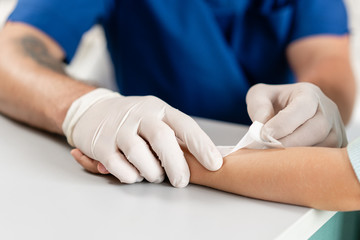 medical patch. Doctor in blue uniform make elastic bandaged around a boy hand with trauma in his...