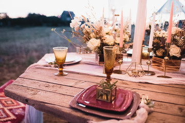Romantic dinner of the bride and groom on a wooden table with burgundy plates and fresh flowers. 