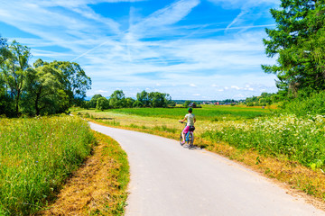 Young woman cyclist standing on cycling way along Dunajec river and looking at green farming fields near Czorsztynskie lake, Pieniny Mountains, Poland